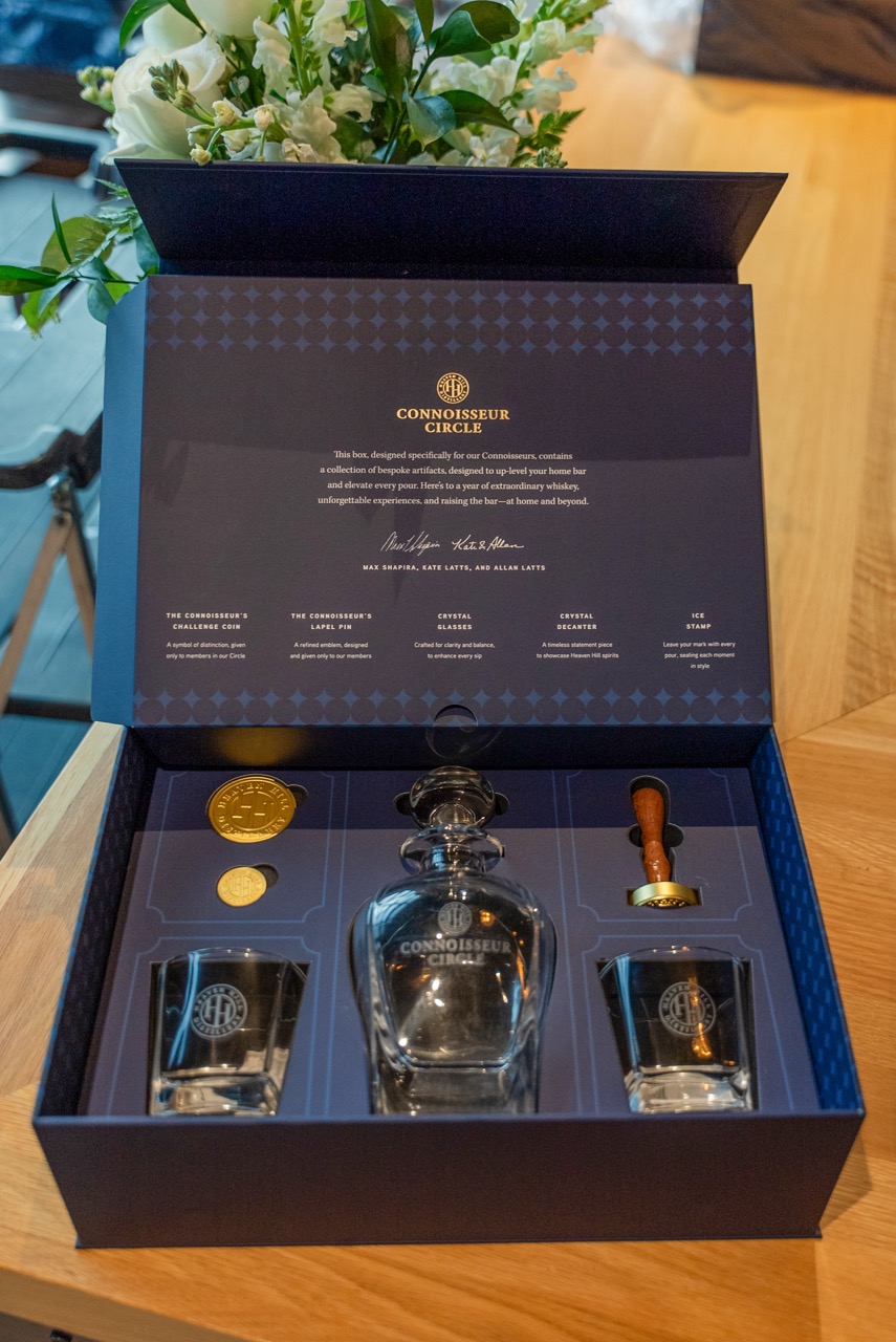 Connoisseur Circle welcome kit open, showing crystal decanter, glasses, challenge coin, and lapel pin